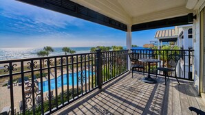 A covered balcony with a view of the ocean, a pool, and outdoor furniture.
