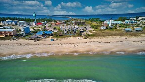 An aerial view of a coastal town with beachfront properties, a lighthouse, and a pier extending into the ocean.