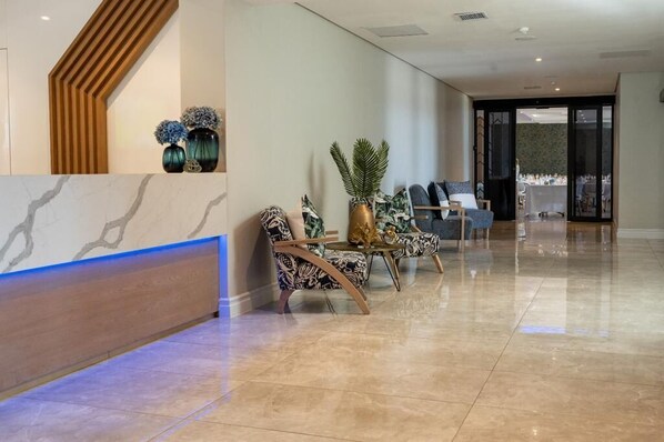 A modern reception area with a marble reception desk, patterned chairs, and a potted plant. - 12 Oceans Hotel and Conference Centre (Kingsburgh)