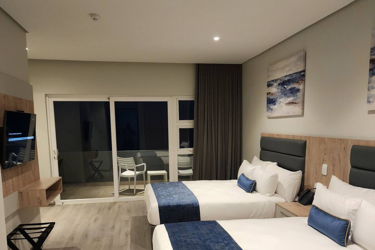A hotel room with two beds, a TV, a desk, and a sliding door to a balcony.