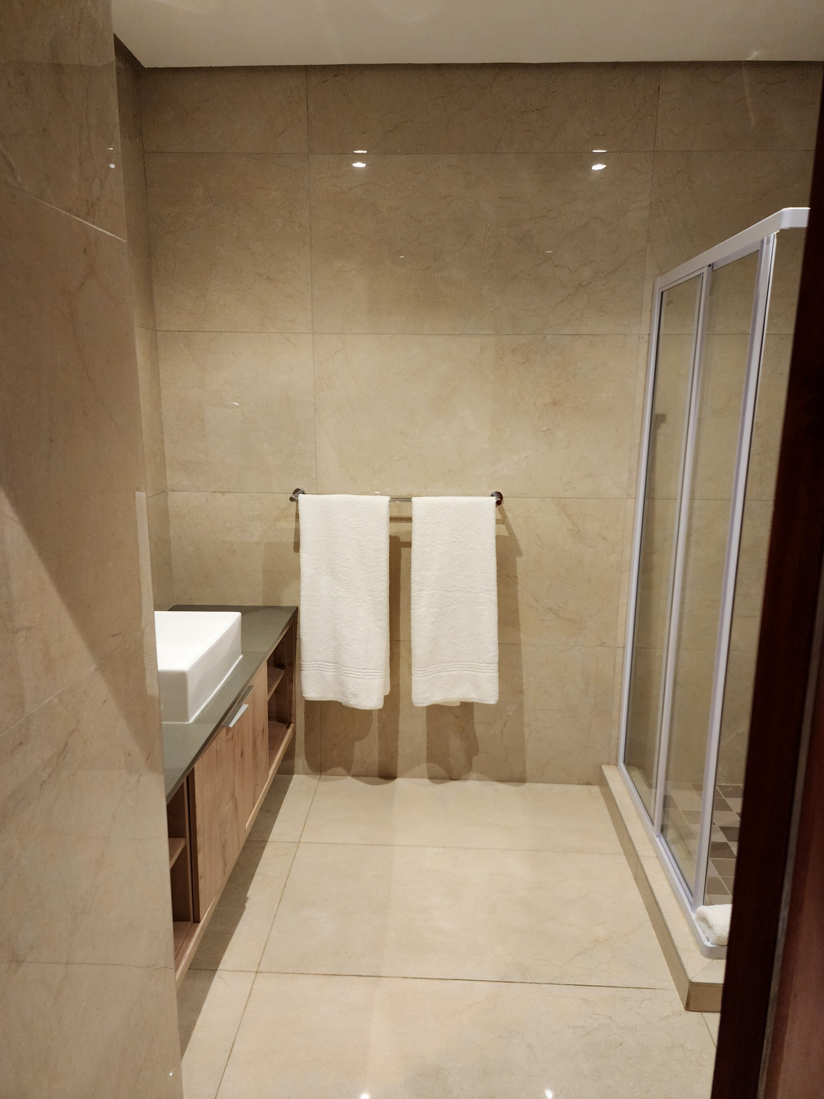 A modern bathroom with a glass shower enclosure, a sink, and two white towels hanging on a rack.