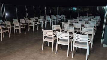An outdoor seating area with rows of white plastic chairs and tables, arranged on a tiled floor.