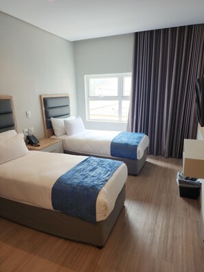 A hotel room with two beds, a window with curtains, a bedside table with a phone, and a trash bin. - 12 Oceans Hotel and Conference Centre (Kingsburgh)
