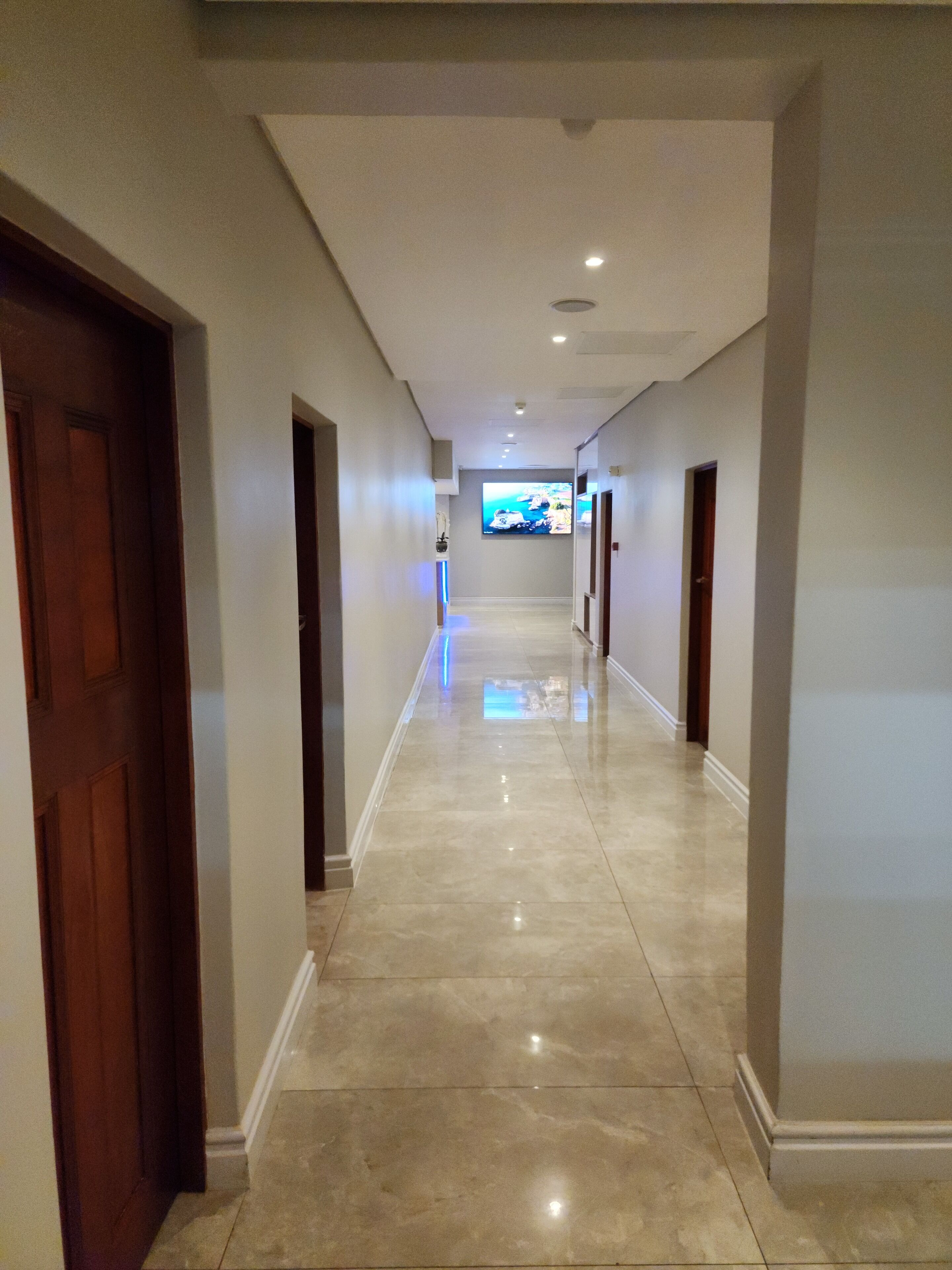 Un pasillo con suelo pulido, puertas de madera y un televisor de pantalla plana montado en la pared.