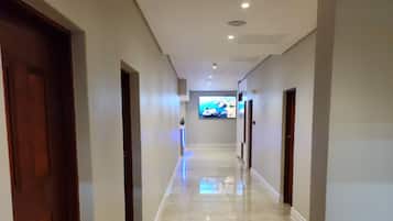 Un pasillo con suelo pulido, puertas de madera y un televisor de pantalla plana montado en la pared.