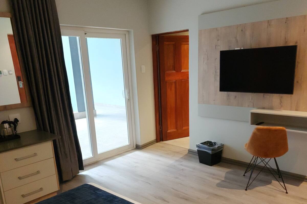 A hotel room with a bed, a desk, a TV, and a sliding door to a balcony.