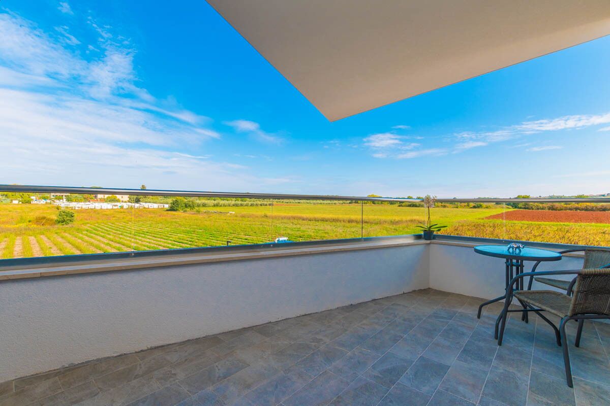 A balcony with a view of agricultural fields, a table, and a chair.