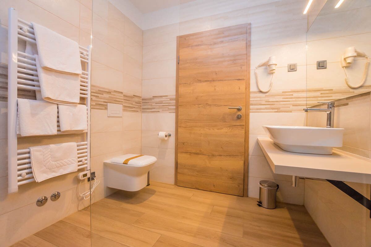 A modern bathroom with a wooden door, a white toilet, a sink with a vessel basin, and a towel rack with folded towels.