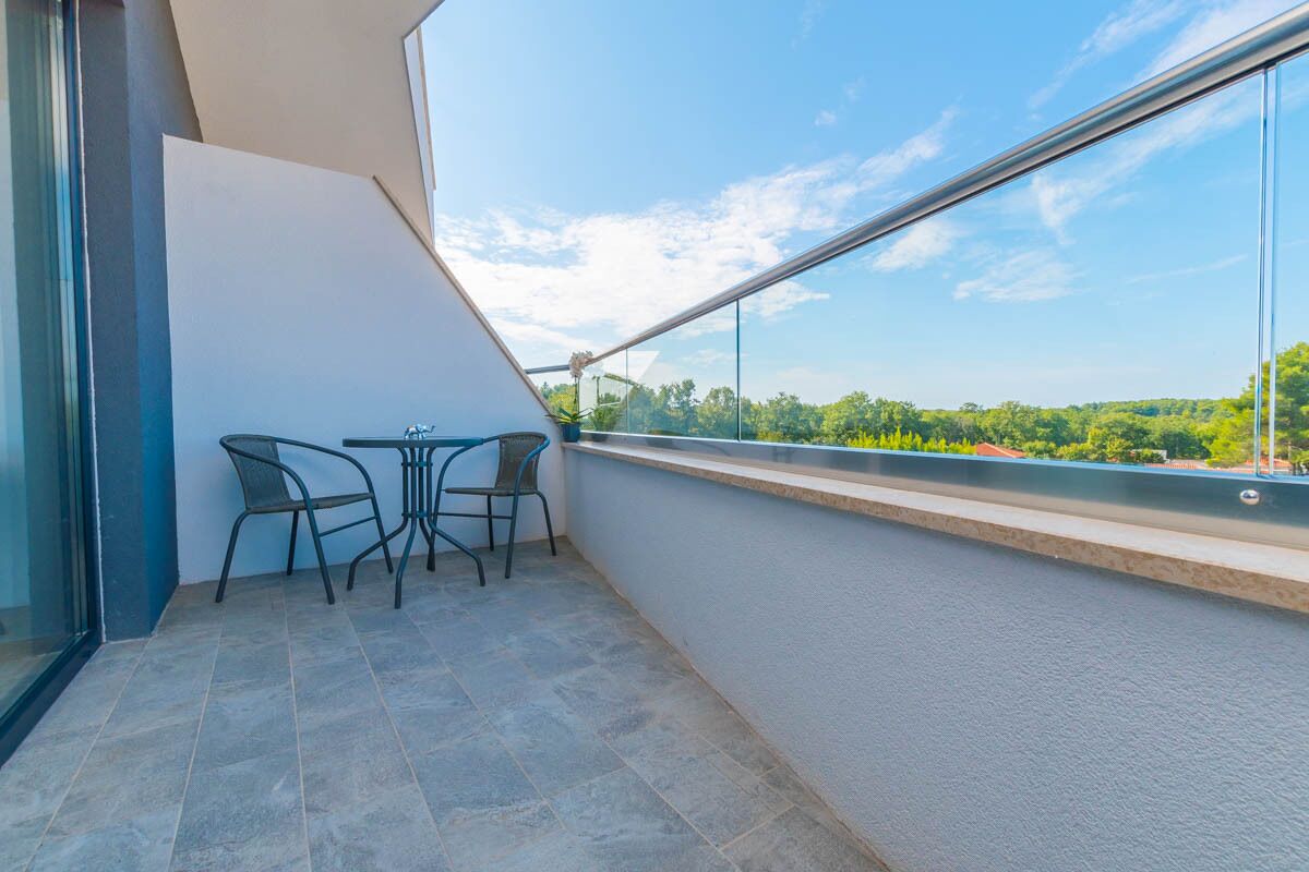 A balcony with two chairs and a small table, overlooking a green landscape.