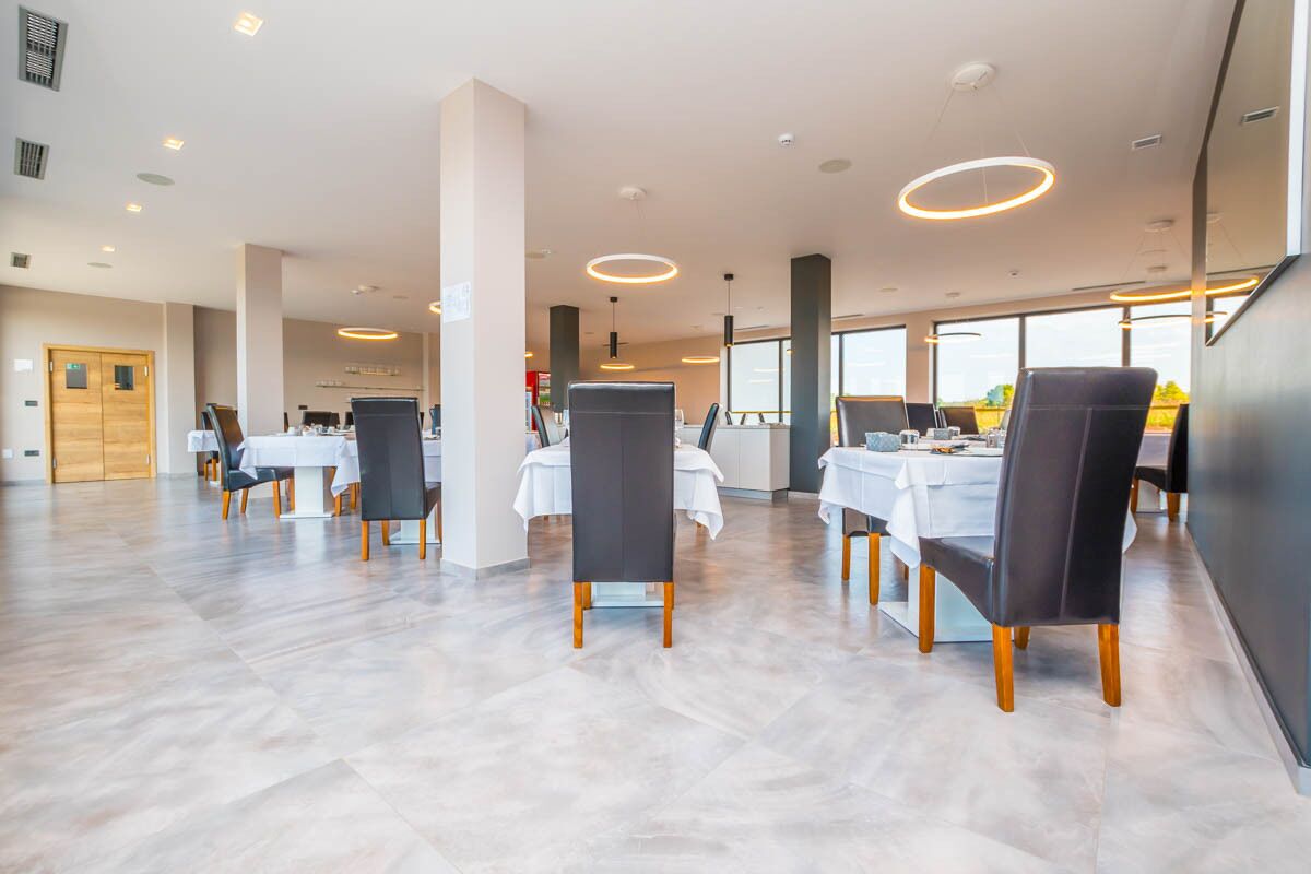 A spacious dining area with multiple tables and chairs, large windows, and a modern ceiling design.