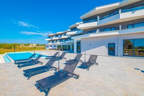 Un hotel moderno con varios balcones, piscina y tumbonas.