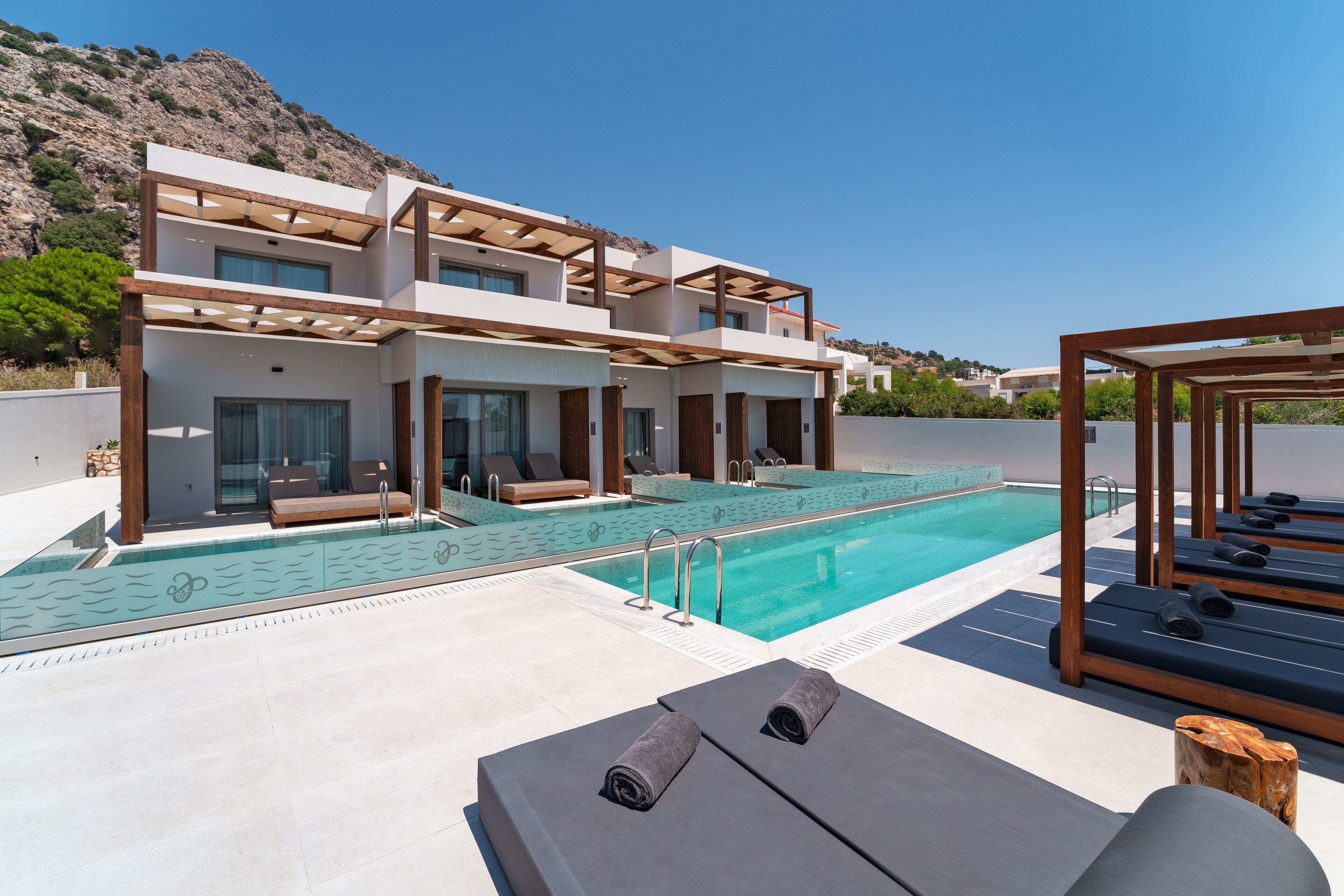 A modern building with a pool, lounge chairs, and a wooden pergola.