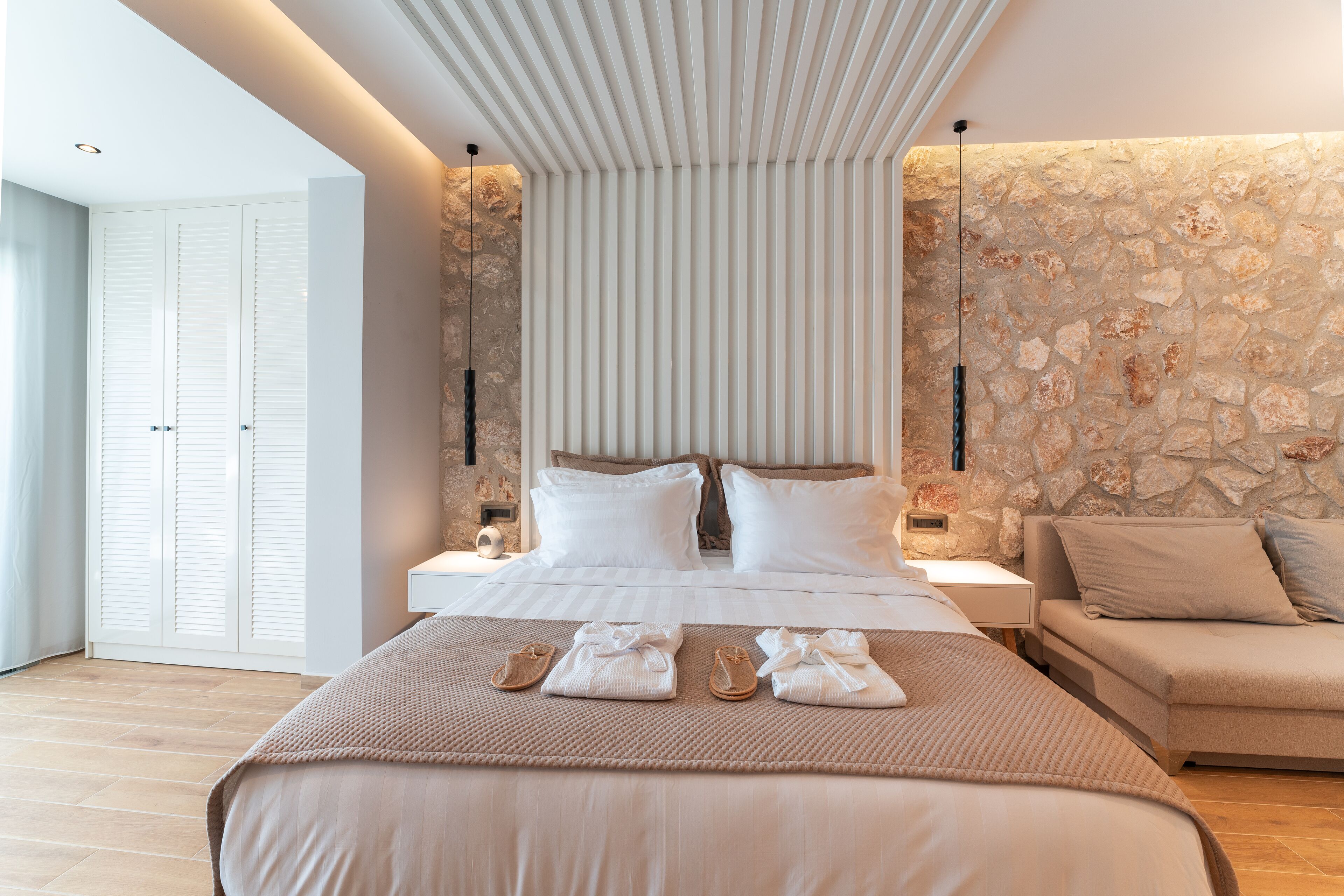 Un dormitorio moderno con una cama grande, una pared decorativa de piedra, una mesita de noche y un sofá.