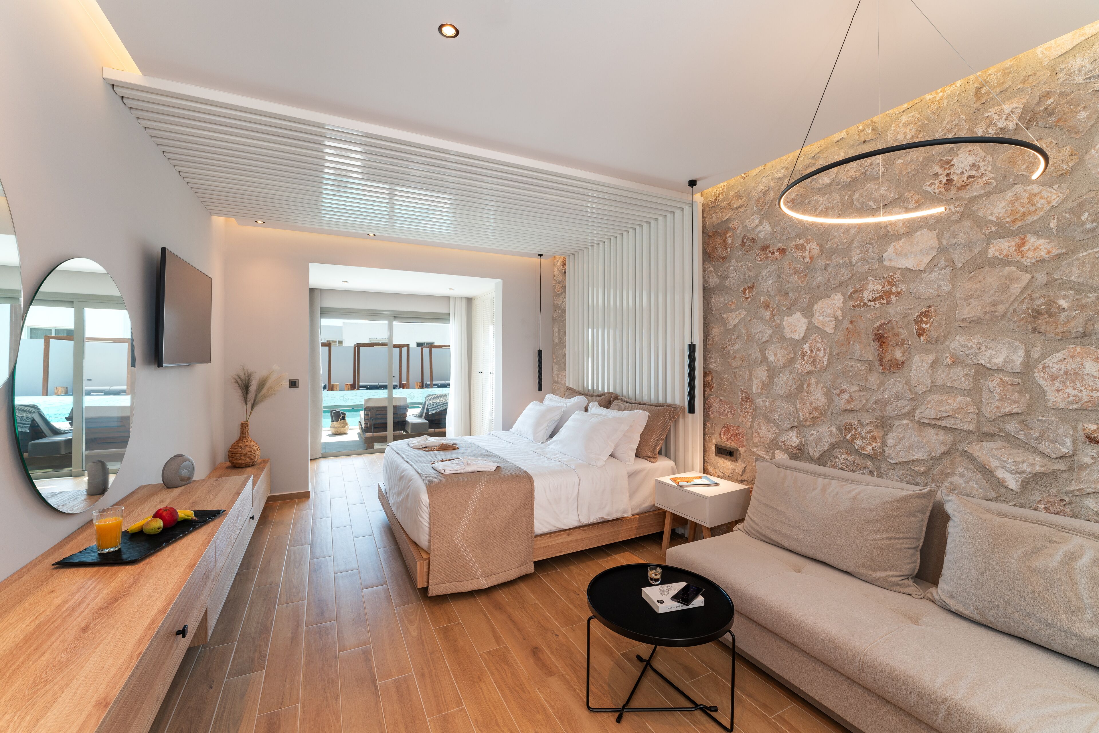A modern bedroom with a bed, a sofa, a small table, and a stone wall.