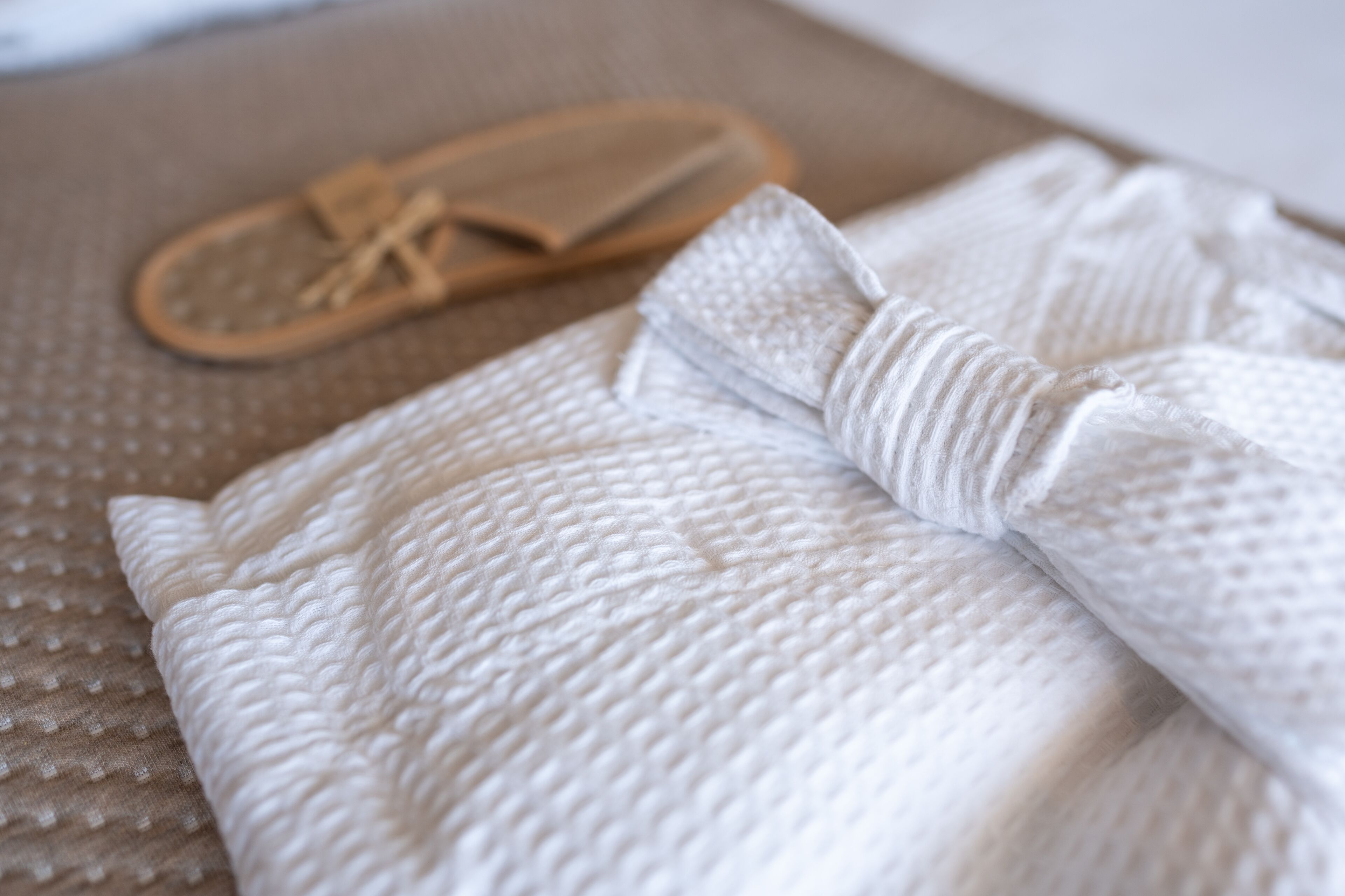 Une serviette blanche soigneusement pliée et une pantoufle en bois reposent sur une surface beige texturée.