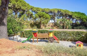 Explore a playground area surrounded by lush trees and a well-maintained hedge, featuring a play structure with a slide, playhouse, and swing set.