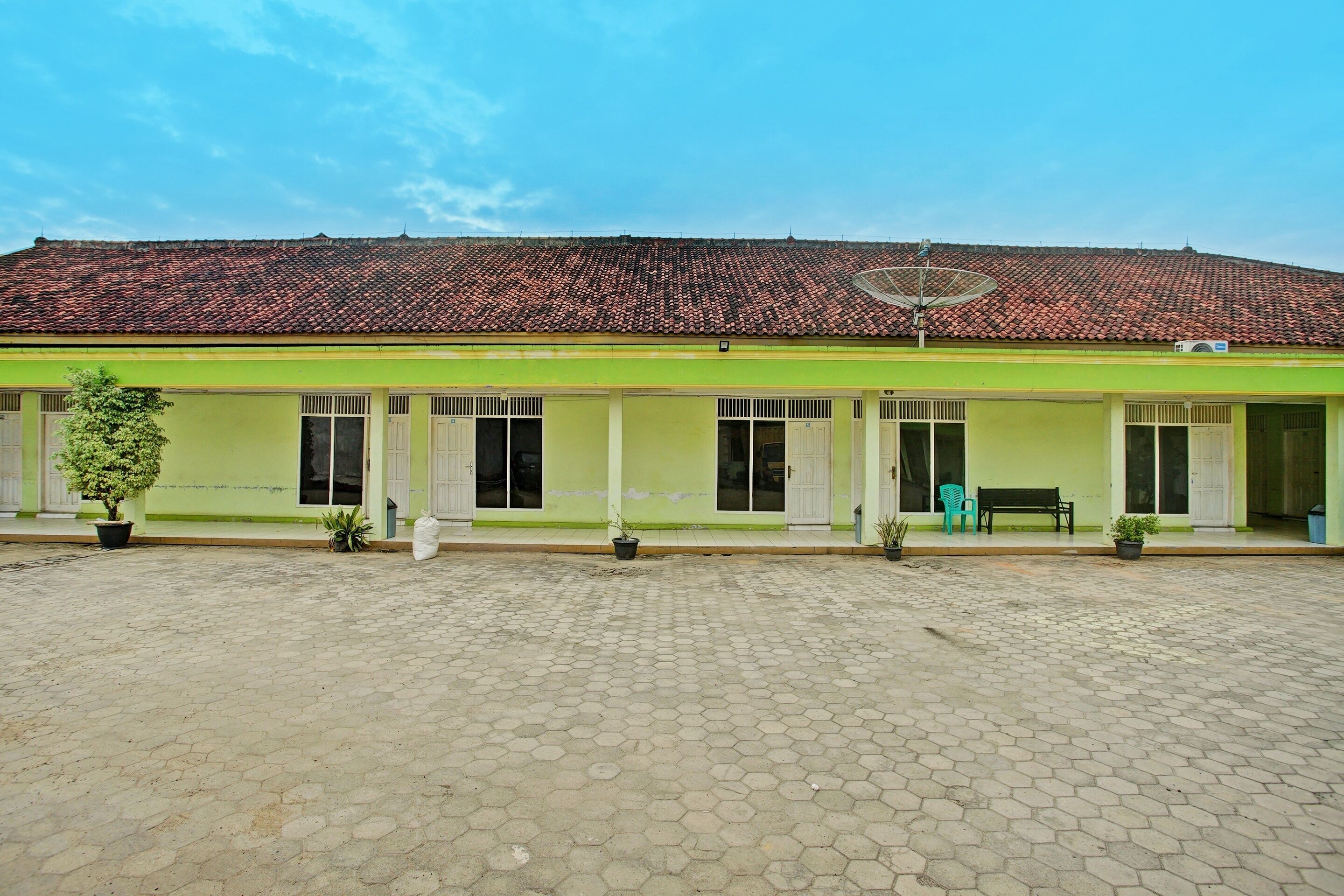 A building with a green facade, a tiled roof, and a paved courtyard.