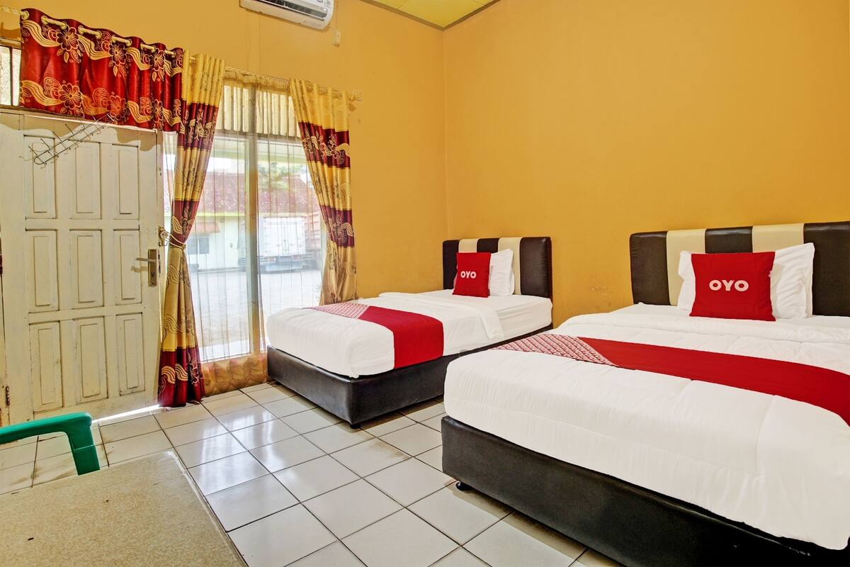 Une chambre d’hôtel avec deux lits, une porte et une fenêtre avec des rideaux.