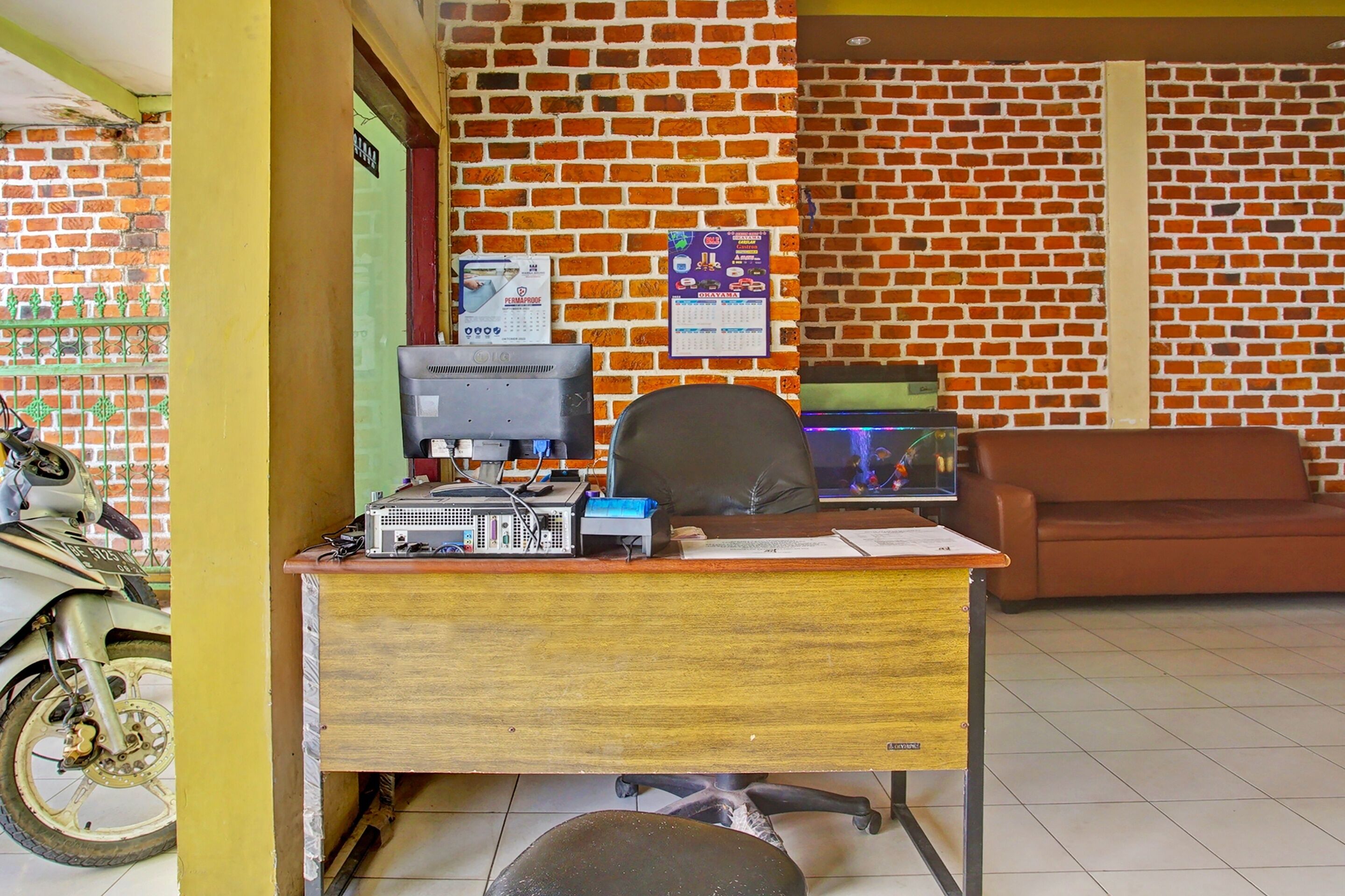 A reception desk with a computer, a chair, and a motorcycle parked outside.