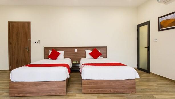 A hotel room with two wooden beds, white bedding, red pillows, and a wooden headboard.