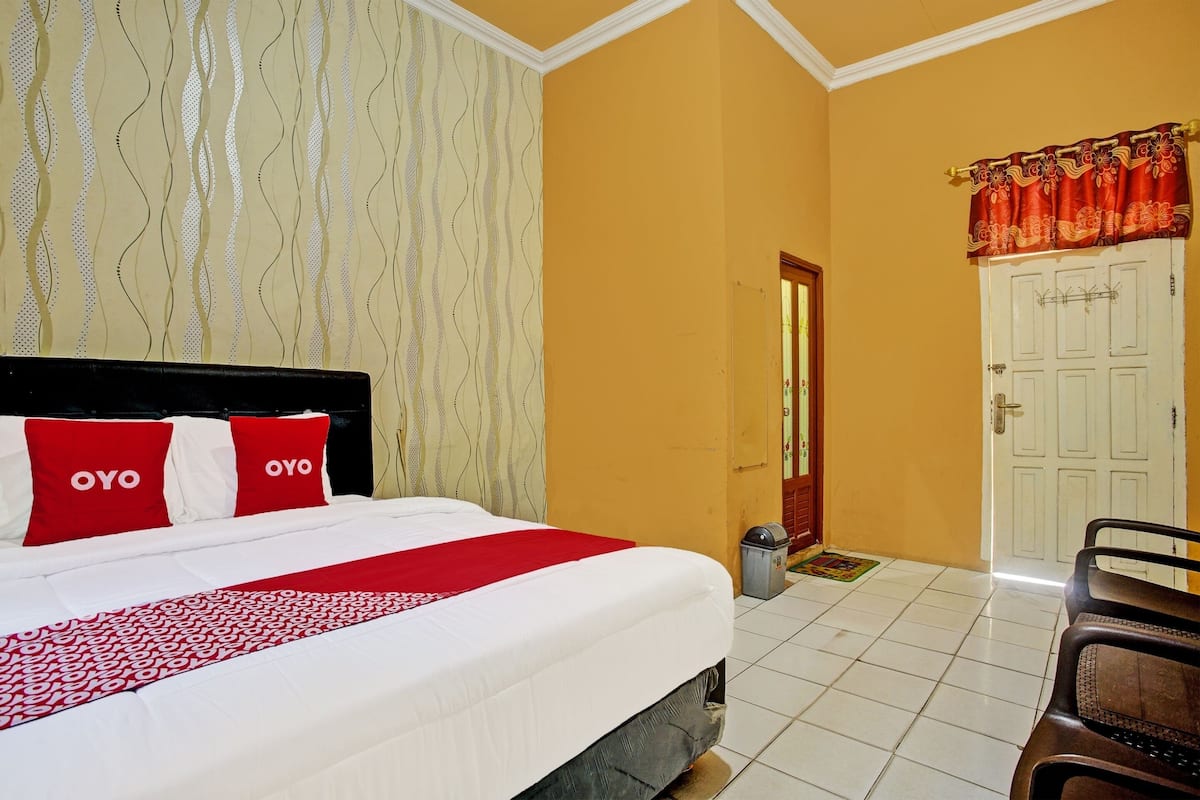 Une chambre d’hôtel avec un lit, une couvre-lit rouge et blanche, un rideau à motifs et une porte blanche.