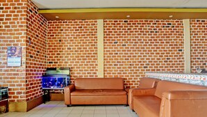 A room with brick walls, a brown leather sofa, a small table with a fish tank, and a tiled floor.