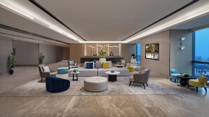 A spacious, modern lounge area with a variety of seating options, a reception desk, and large windows offering a view of the city. - Somerset Taihu New City CBD Wuxi (Wuxi)