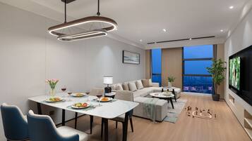 A modern living room with a dining area, a sofa set, a flat-screen TV, and a large window with a city view.