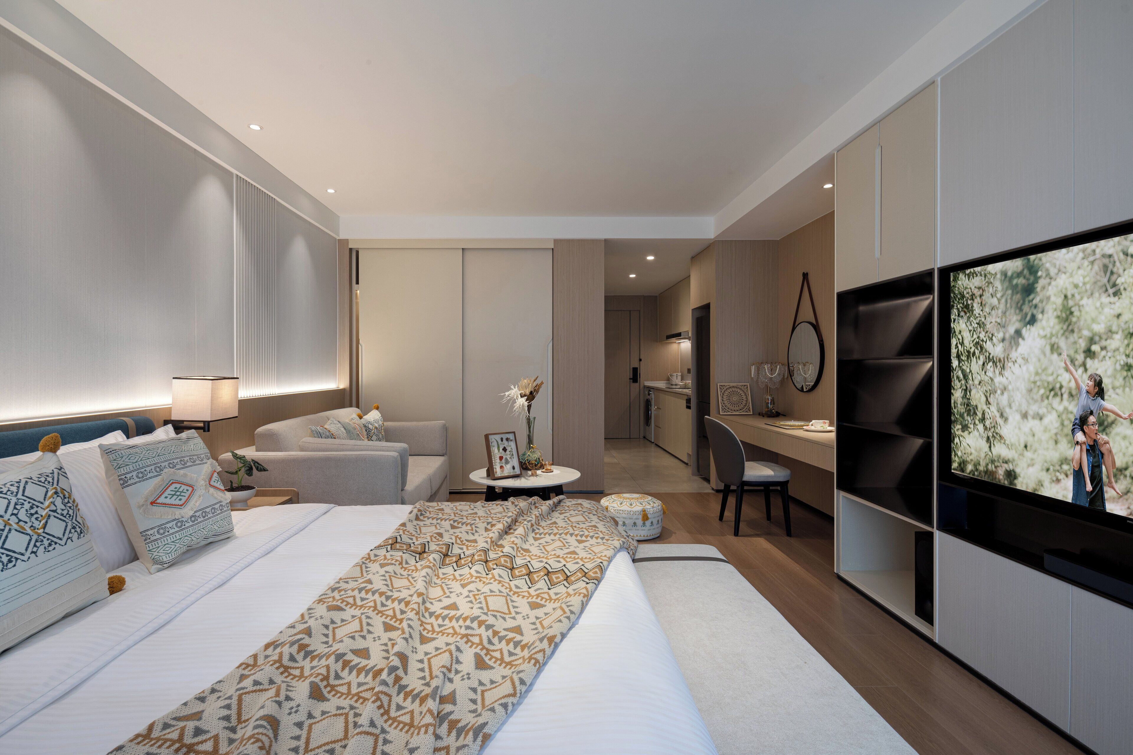 Quarto de hotel moderno com cama grande, televisão, área de estar e cozinha compacta.
