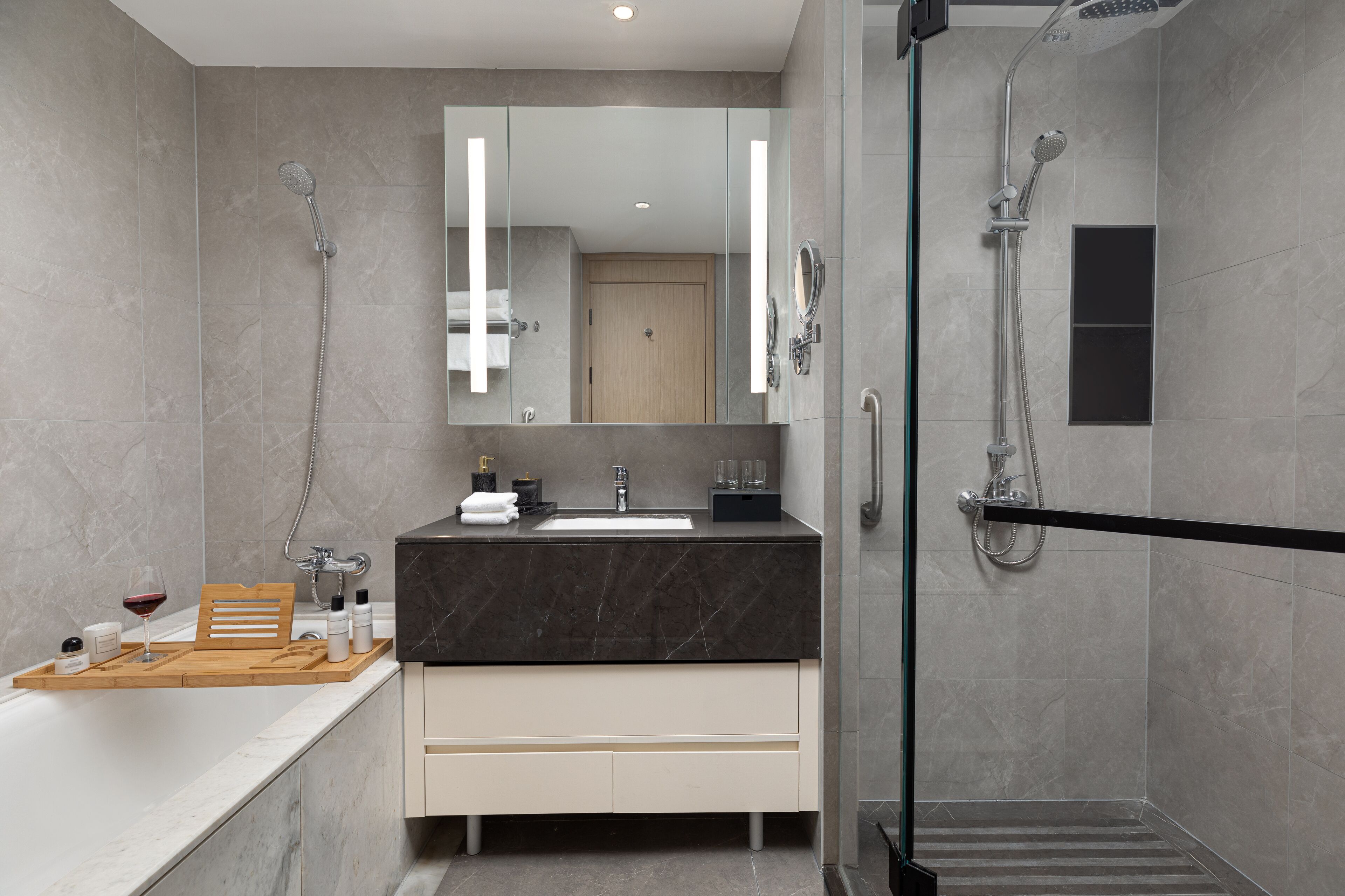 Une salle de bain moderne avec un meuble-lavabo en marbre, une cabine de douche en verre et un plateau en bois contenant des articles de toilette.