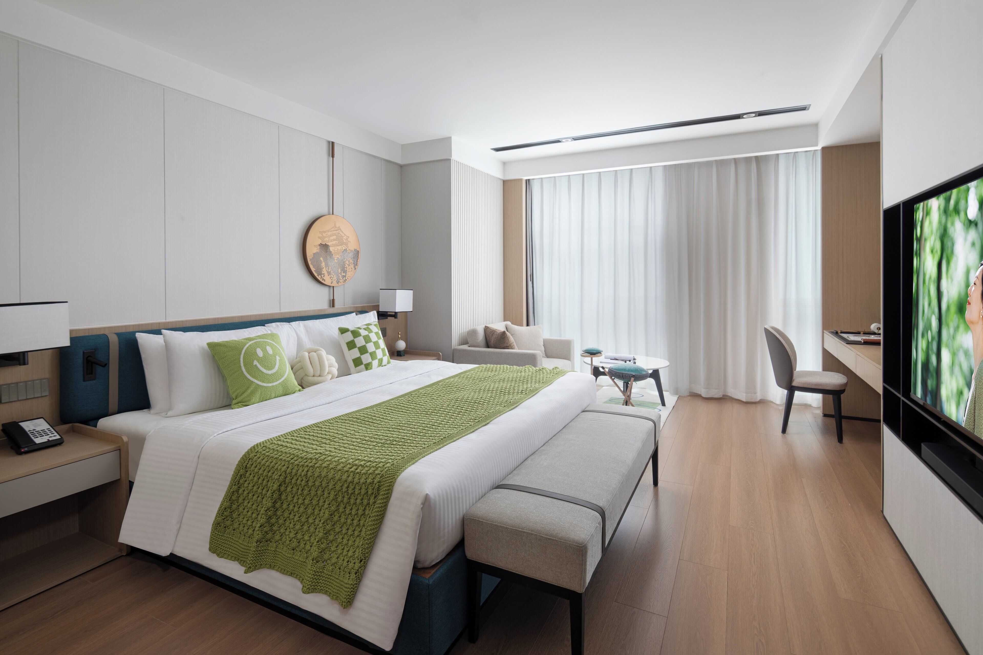 A modern hotel room with a large bed, a desk, a chair, a TV, and a window with curtains.