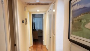 Un couloir avec un sol carrelé, des murs blancs et un tableau encadré sur le côté droit.