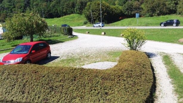 Une allée de gravier mène à un espace de stationnement où une voiture rouge est garée sur le côté gauche.