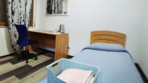 Une petite pièce bien rangée, avec un lit simple, un bureau et une chaise.