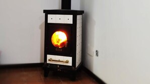 Un poêle à bois doté d’une porte en verre, d’une poignée en laiton et d’une petite étagère située sous la porte.