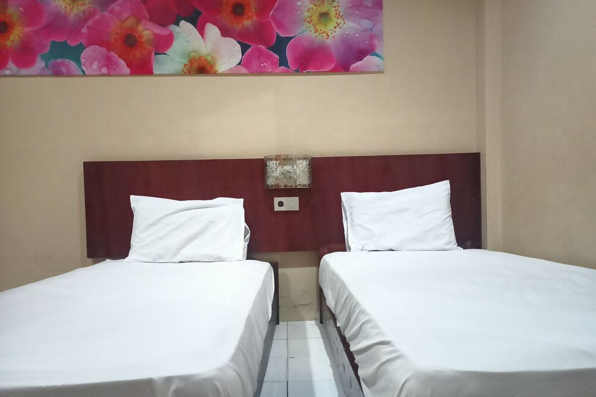 Une chambre d’hôtel avec deux lits simples, une tête de lit en bois, une œuvre d’art accrochée au mur et une petite table de chevet.