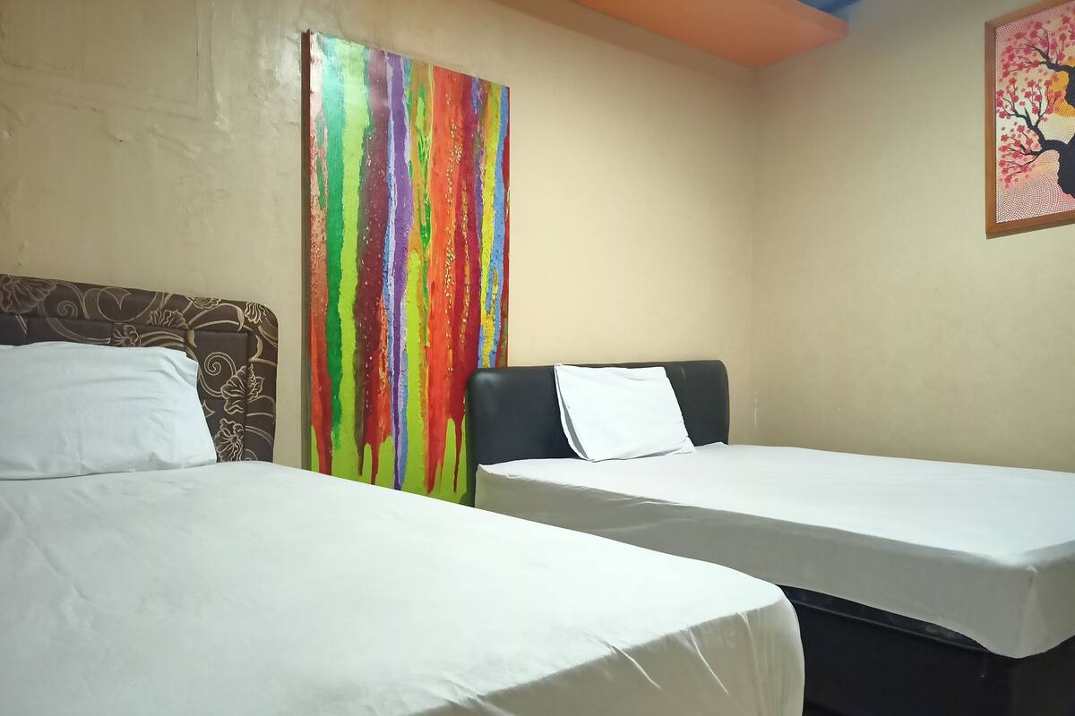 Une chambre d’hôtel avec deux lits, une peinture abstraite aux couleurs vives accrochée au mur et un tableau encadré au-dessus des lits.