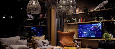 Una sala de estar moderna con sofá, sillón y mesa de centro, televisor y plantas decorativas.