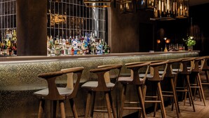 Una zona de bar con una barra larga, varios taburetes y una amplia variedad de botellas.