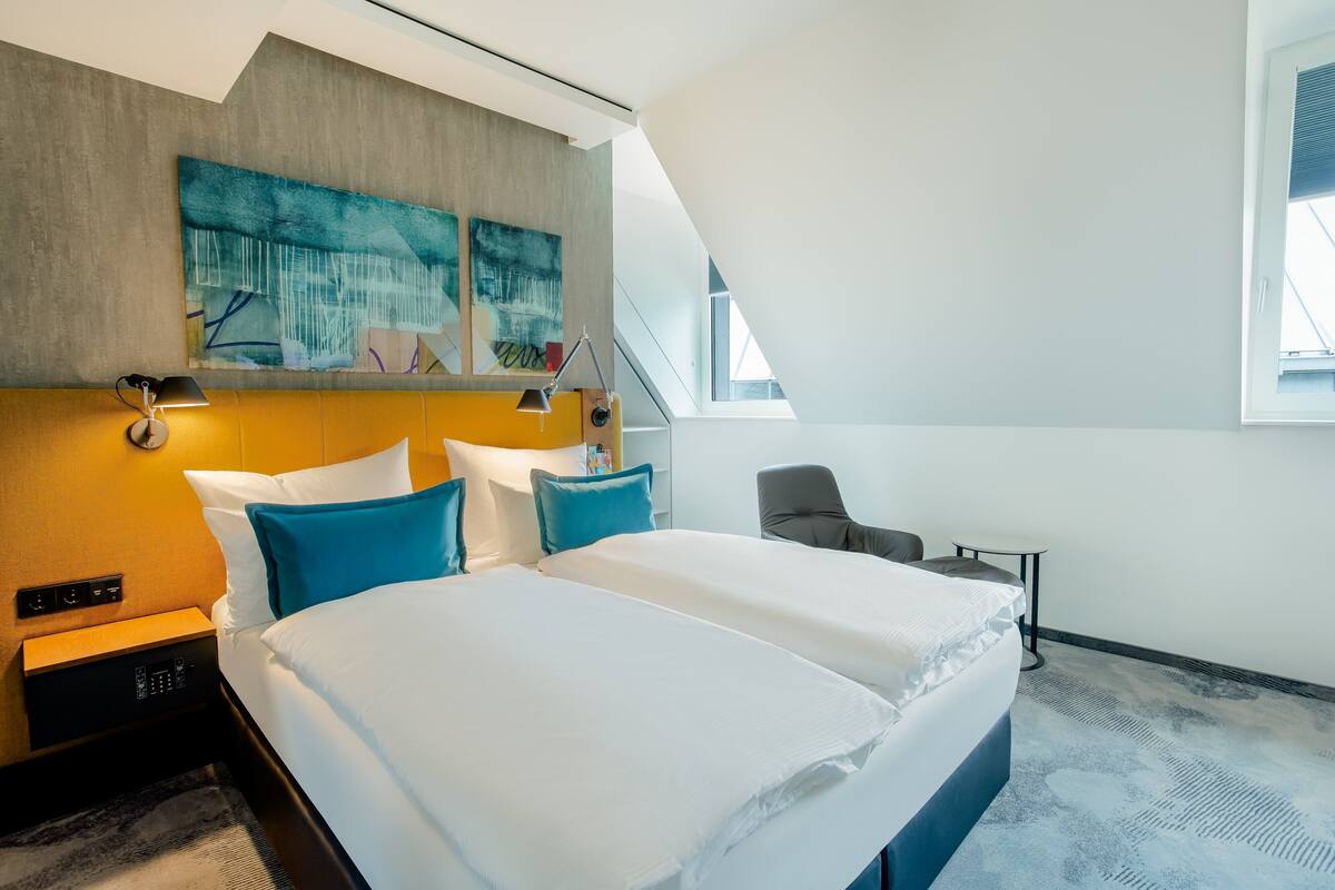 Habitación de hotel moderna con una cama grande, un escritorio y una silla. Hay un cuadro en la pared y una ventana con vistas al exterior.