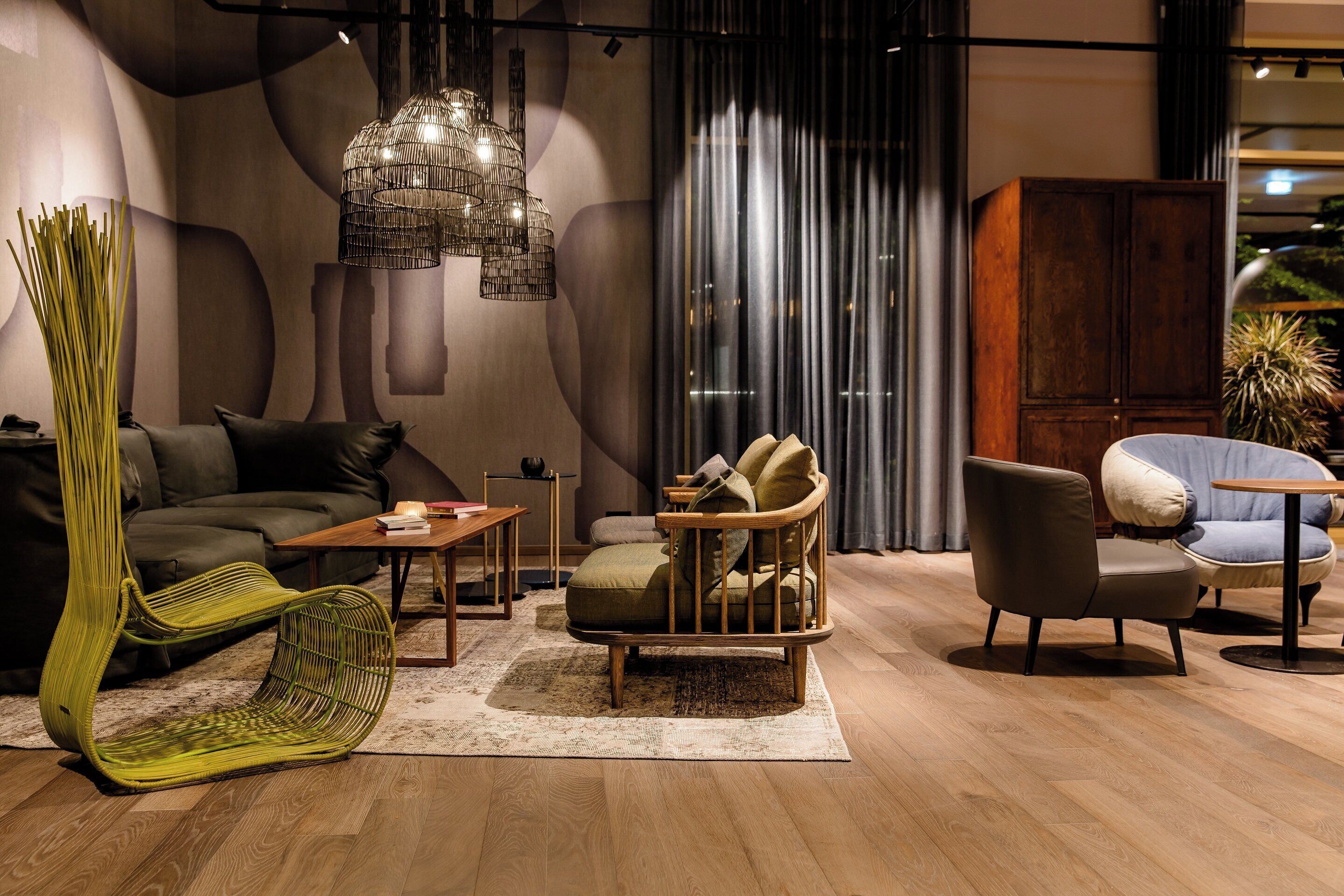 A modern living room with a sofa, a green chair, a wooden coffee table, and a hanging light fixture.