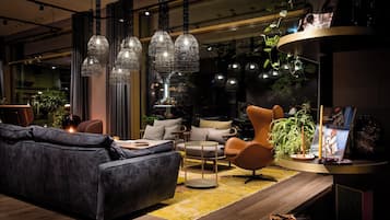 A modern living room with a dark grey sofa, a round coffee table, and a yellow rug. There are pendant lights hanging from the ceiling and a plant on a side table.