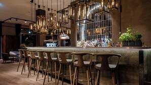 Un área de bar con taburetes de madera, lámparas colgantes y una variedad de botellas sobre la barra.