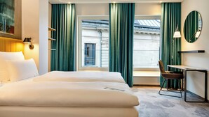 Habitación de hotel con una cama grande, un escritorio con silla, una ventana con cortinas y una lámpara de pared.