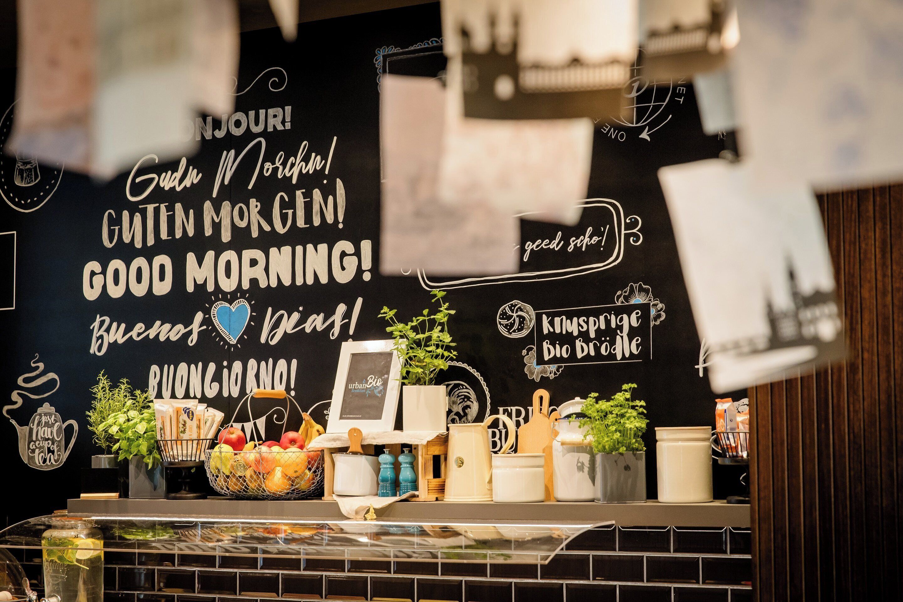 A breakfast bar with a chalkboard wall displaying various breakfast-related phrases and a selection of fresh fruits, eggs, and cooking utensils.