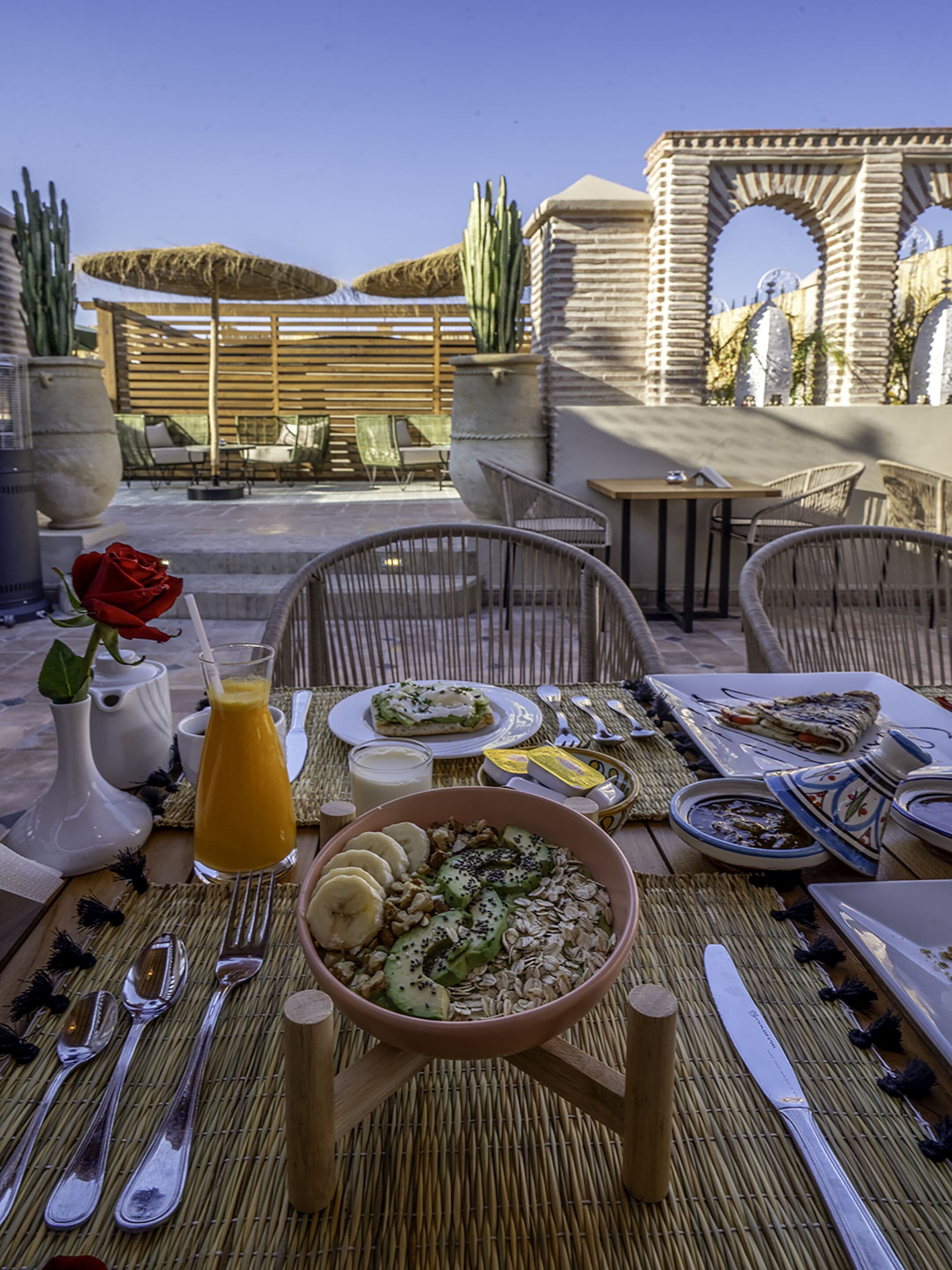 Een terras met een ontbijt, inclusief een kom cerea, een glas sinaasappelsap en borden met eten.