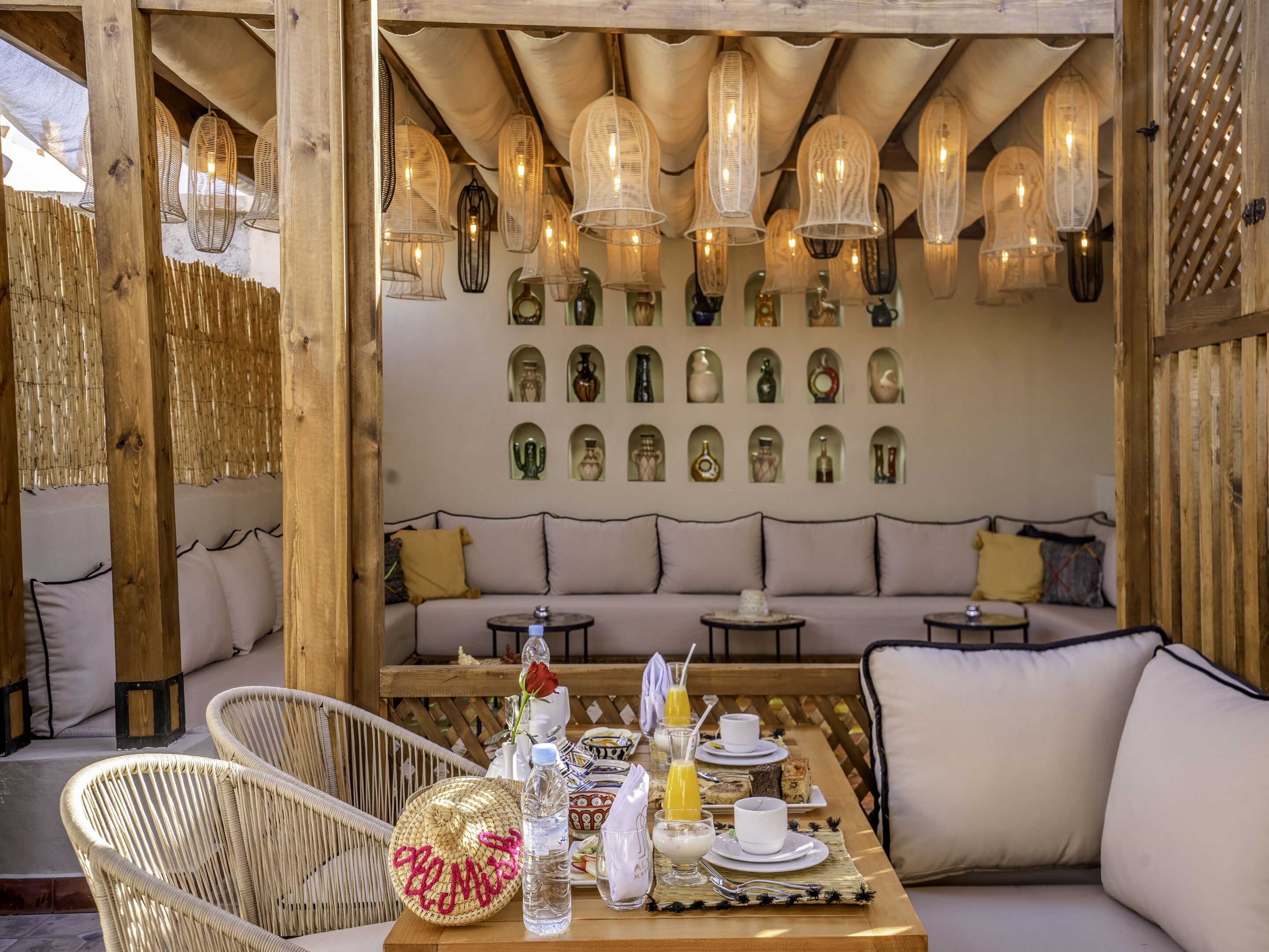A cozy outdoor seating area with wicker chairs, a wooden table set with breakfast items, and a wall of decorative vases.