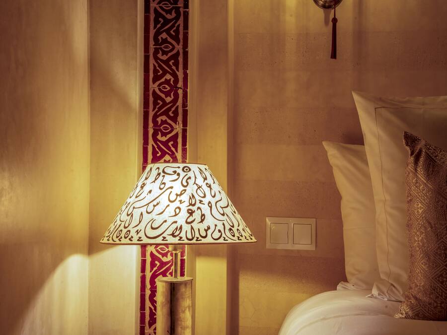 Una habitación con una cama, una lámpara de diseños intrincados y una pared con azulejos decorativos.