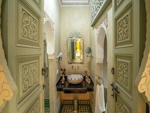 A bathroom with ornate doors, a sink with a bowl, a mirror, and a shower.