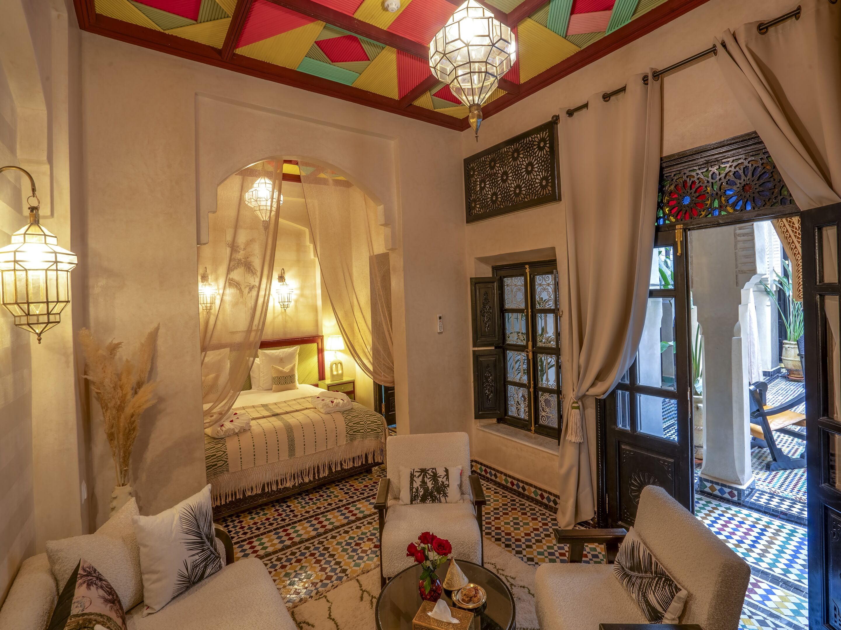 A room with a bed, a sitting area with a coffee table, and a view of the outside.
